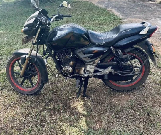 The black TVS Apache 150 on its side stand on grass, red-rimmed wheels, nine years of city commuting on it