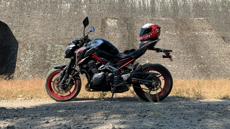 The black and red Kawasaki Z900 against a stone fort wall, a Venom-graphic helmet resting on the tail