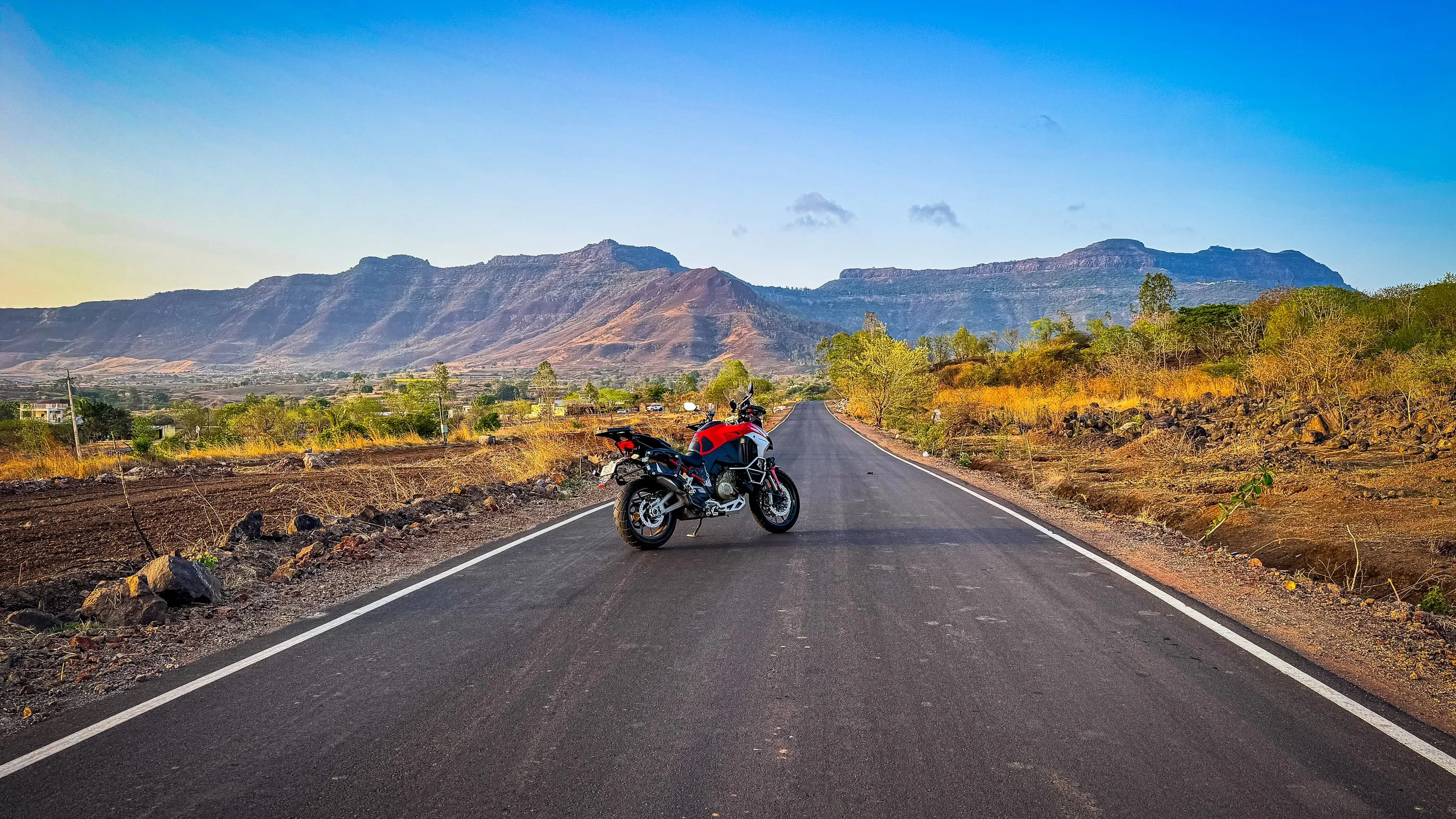 The Ducati Multistrada V4 parked on an empty road running towards a range of flat-topped hills, late afternoon light